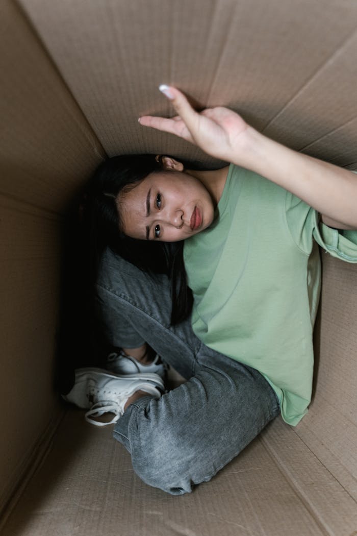 A woman in a cardboard box showing signs of anxiety or claustrophobia.