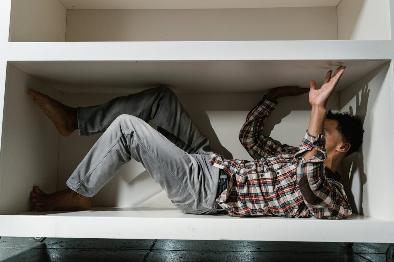 A man in a plaid shirt exhibits claustrophobia while inside a small cabinet, evoking emotions of anxiety and fear.
